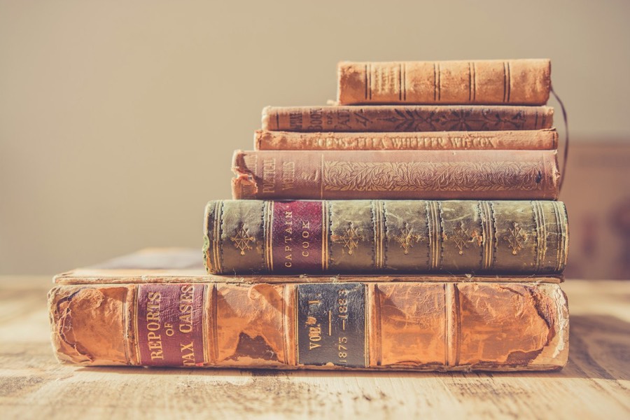 A stack of old leather-bound books on a wooden table