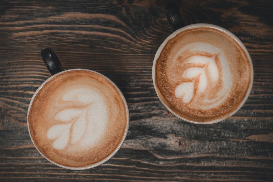 Two cappuccinos side by side on a wooden table